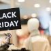 Background image of Black Friday sign on clothes rack with autumn clothes in shopping mall during sale season, copy space