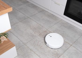 Washing White robot vacuum cleaner on a concrete tile floor cleaning dust in a Scandinavian loft minimalist kitchen interior. Smart Electronic Household Technology.