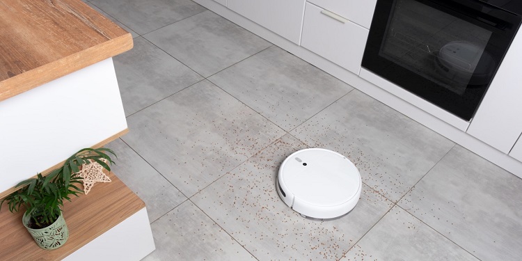 Washing White robot vacuum cleaner on a concrete tile floor cleaning dust in a Scandinavian loft minimalist kitchen interior. Smart Electronic Household Technology.