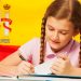 Diligent teenage student, Caucasian girl, writing with a pen in her copybook, Spanish flag behind
