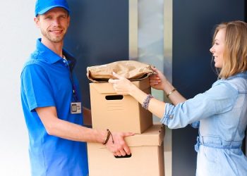 Smiling delivery man in blue uniform delivering parcel box to recipient - courier service concept. Smiling delivery man in blue uniform.