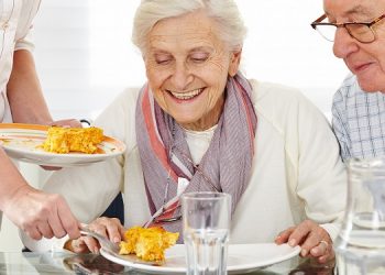 Zwei lächelnde Senioren essen Lunch im Pflegeheim