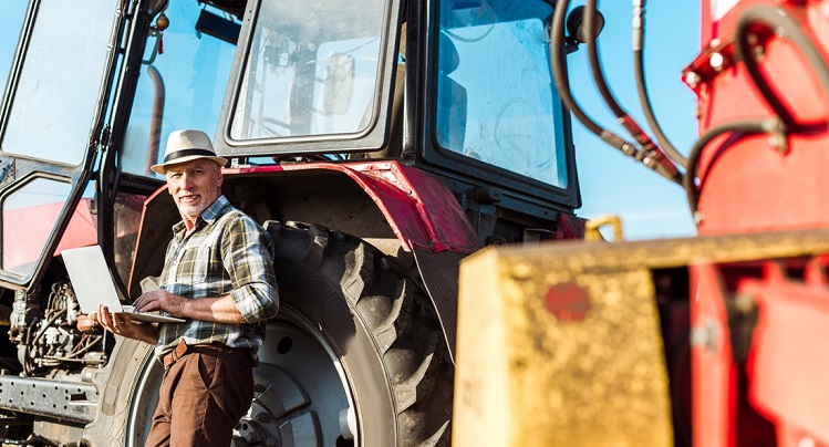 selective focus of happy farmer in straw hat using laptop near tractor