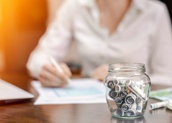 jar with rolled banknotes table laptop papers woman background