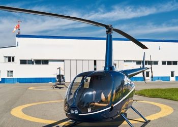 Empty rotary-wing aircraft standing on concrete landing pad before metal hangar at heliport