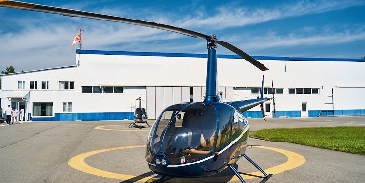 Podnajem prywatnego helikoptera - jak zarabiać na własnej maszynie? 1 Empty rotary-wing aircraft standing on concrete landing pad before metal hangar at heliport