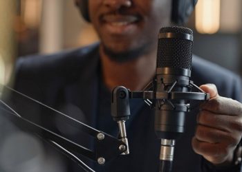 Close up shot of professional condenser microphone and African American male hand setting it up during live podcast in studio